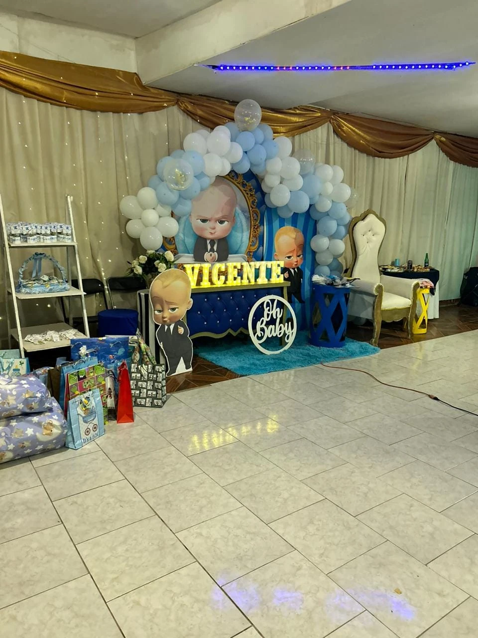 Montaje de celebración con globos azules, blancos y dorados, pequeños pedestales y detalles infantiles.