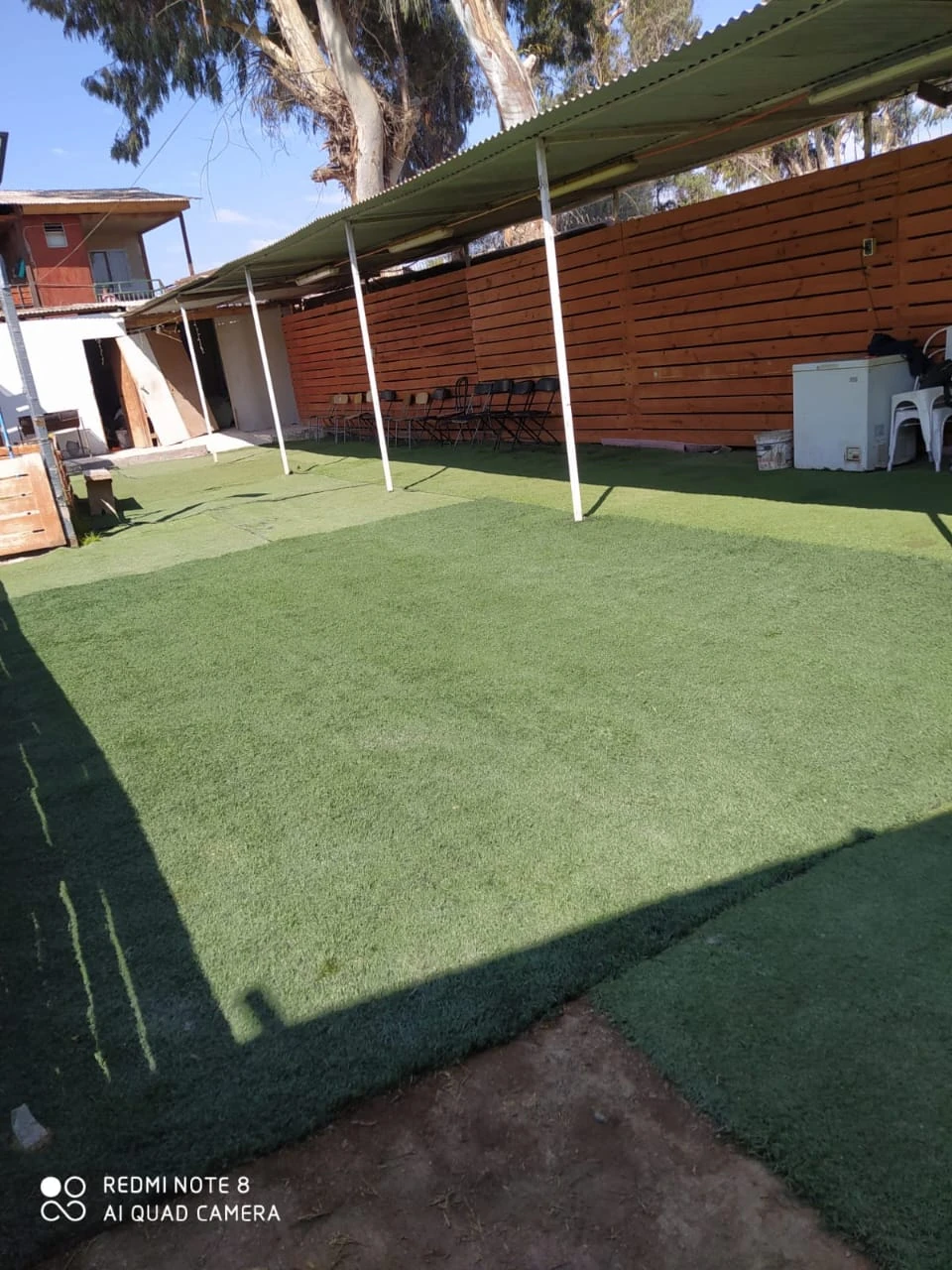 Área exterior de Manantial con césped, árboles y construcciones de madera alrededor.