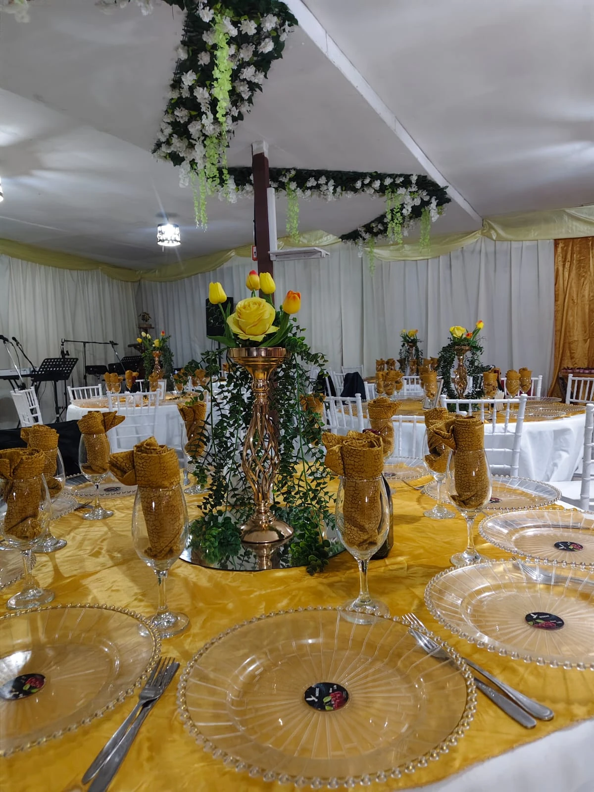 Mesa preparada con mantelería dorada, copas, platos transparentes y un centro floral con girasoles.