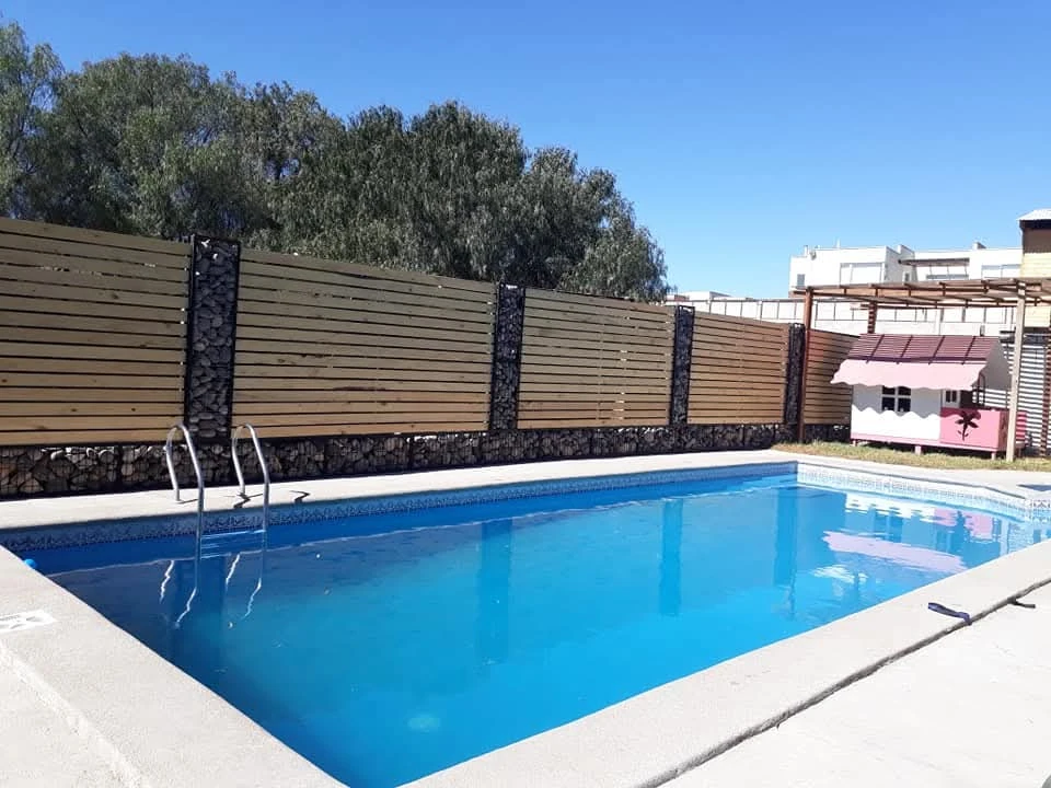 Vista diurna de una piscina azul en Manantial, junto a una cerca de madera y bajo un cielo despejado.